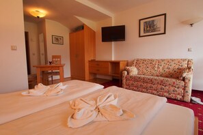 A hotel room with two beds, a wooden wardrobe, a floral sofa, a television, and a framed picture on the wall.