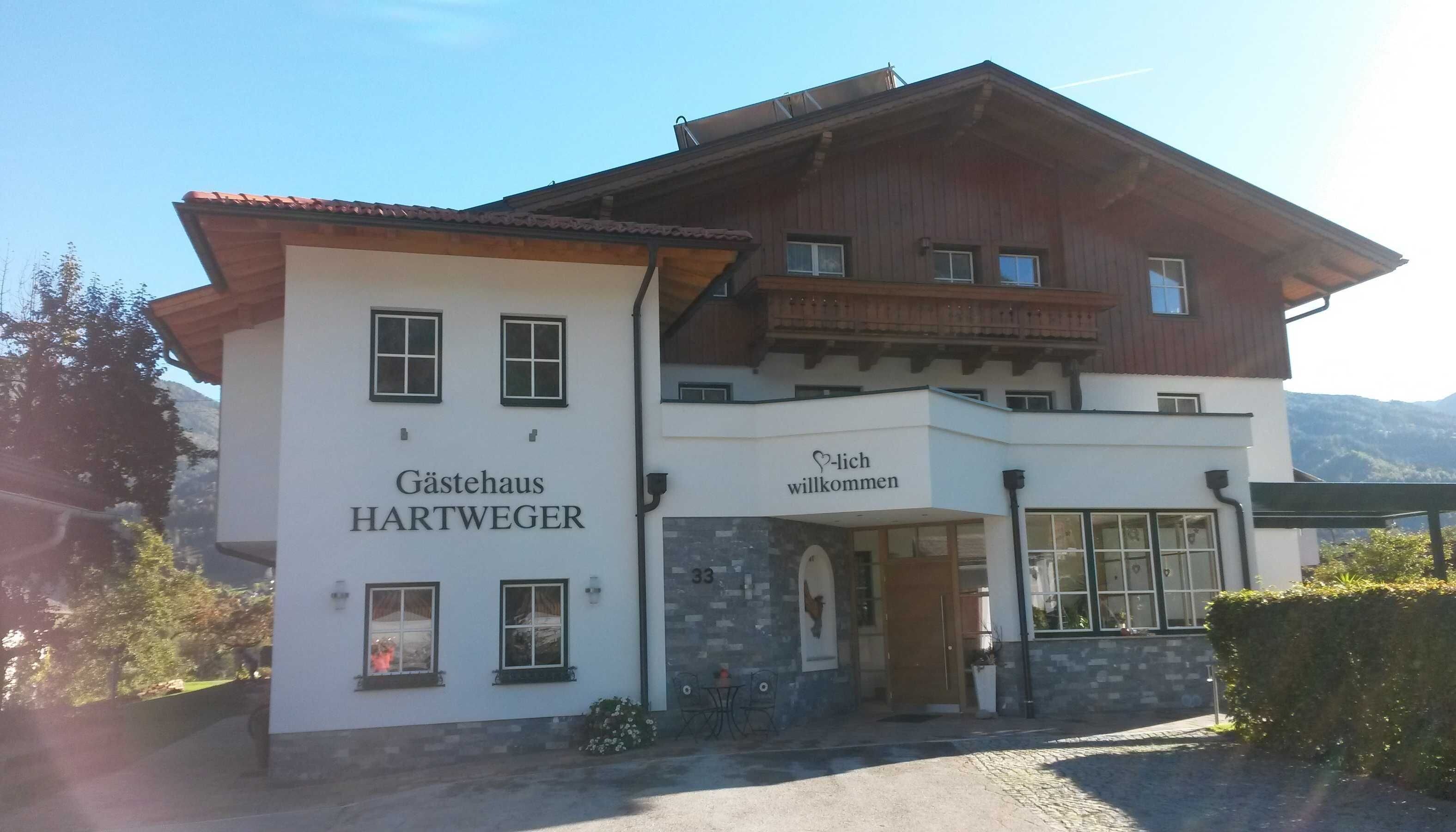 Ein zweistöckiges Gebäude mit einem Schild, auf dem 'Gästehaus HARTWEGER' und 'Willkommen' stehen, das ein Gästehaus kennzeichnet.