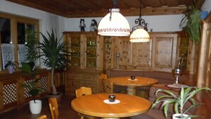 A wooden interior with round tables and chairs, potted plants, and a decorative ceiling light. - Apartment Kufstein, Luser - guest house Hartweger (Weißenbach)