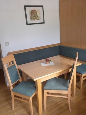 A dining area with a wooden table and four chairs, a small potted plant on the table, and a framed picture on the wall.