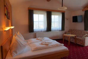 Hotellihuone, jossa on sänky, sohva, pieni pöytä, televisio ja ikkuna, jossa on verhot.