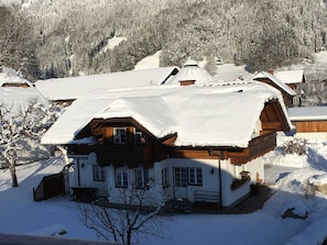 Lumipeitteinen alppimaja, jossa on kalteva katto, puinen ulkoverhous ja useita ikkunoita.