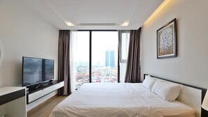 A hotel room with a bed, a TV, a desk, and a large window with a city view.