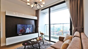 A modern living room with a flat-screen TV, a sofa, a coffee table, and a balcony with a city view.