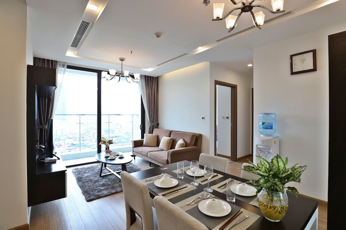 A modern living room with a sofa, dining table set for four, and a large window offering a city view.