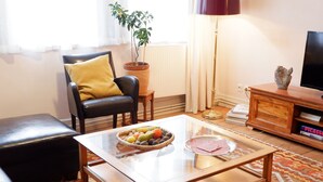 A living room with a leather sofa, a wooden coffee table with fruit, a potted plant, a floor lamp, and a bookshelf with books. - In the middle of Tübingen's old town - and live quietly on a sunny 65 sqm! (Tübingen)