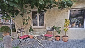 An outdoor seating area with a round metal table and two chairs, surrounded by potted plants and a stone bench. - In the middle of Tübingen's old town - and live quietly on a sunny 65 sqm! (Tübingen)