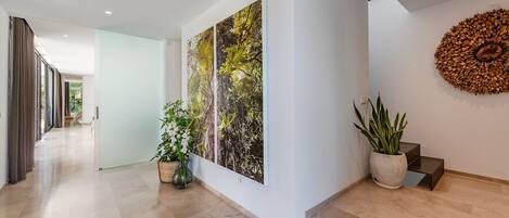 A modern hallway with a wooden floor, a large painting of trees, a potted plant, and a unique wooden wall decoration.