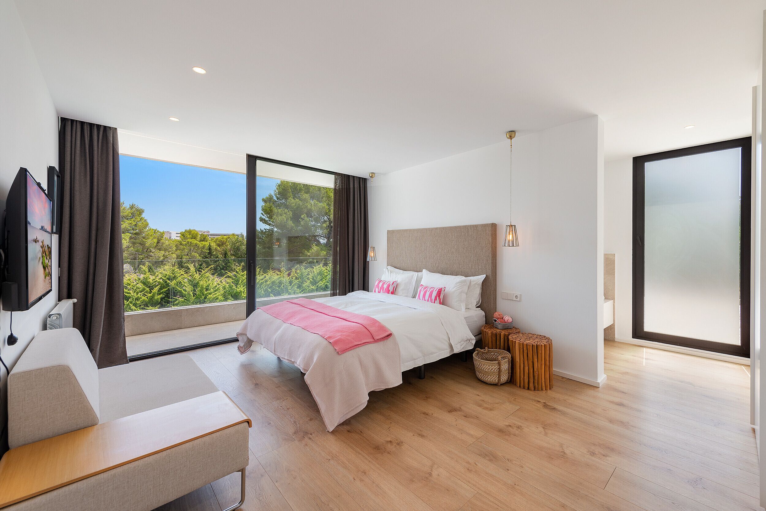 Quarto moderno com uma cama grande, uma escrivaninha e vista para o verde pela janela.