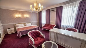A hotel room with a large bed, a sitting area with a red armchair, a small round table, and a white cabinet. - Hotel Orto-Asia (Osh)