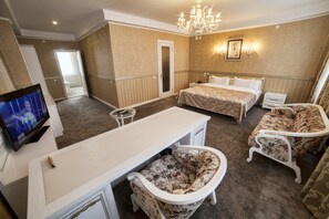 Una habitación de hotel con cama, escritorio, silla, televisor y candelabro.
