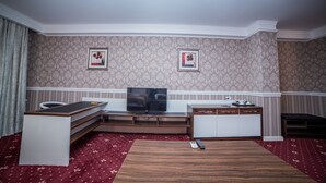 A hotel room with a wooden coffee table, a television on a stand, a small cabinet, and a patterned carpet. - Hotel Orto-Asia (Osh)