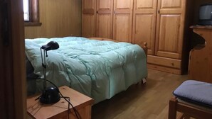 Ein Schlafzimmer mit einem Bett, einem Schreibtisch mit Lampe, einem Fernseher und Holzschränken.