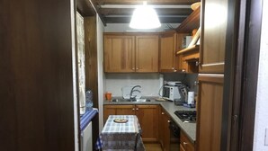 Eine kleine Küche mit Holzschränken, einem Tisch mit kariertem Tischläufer, einem Spülbecken und einfachen Geräten.
