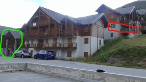 Un hotel con varios balcones, zona de estacionamiento y un paisaje montañoso de fondo.
