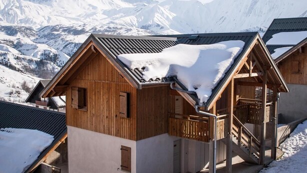 Una cabaña de madera con balcón y escalera, con una imponente montaña nevada de fondo.