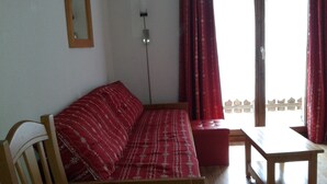 Una habitación con un sofá de madera, una mesita y una ventana con cortinas rojas.