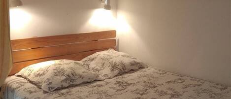 A bed with a wooden headboard, two wall-mounted lamps, and a floral-patterned bedspread.