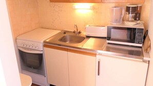 Una kitchenette compacta con estufa, fregadero, microondas y tostadora.