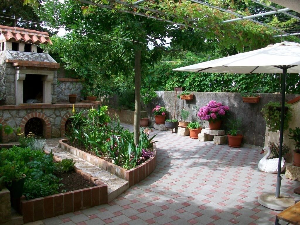 A patio with potted plants, a swan statue, and a stone building with a tiled floor.