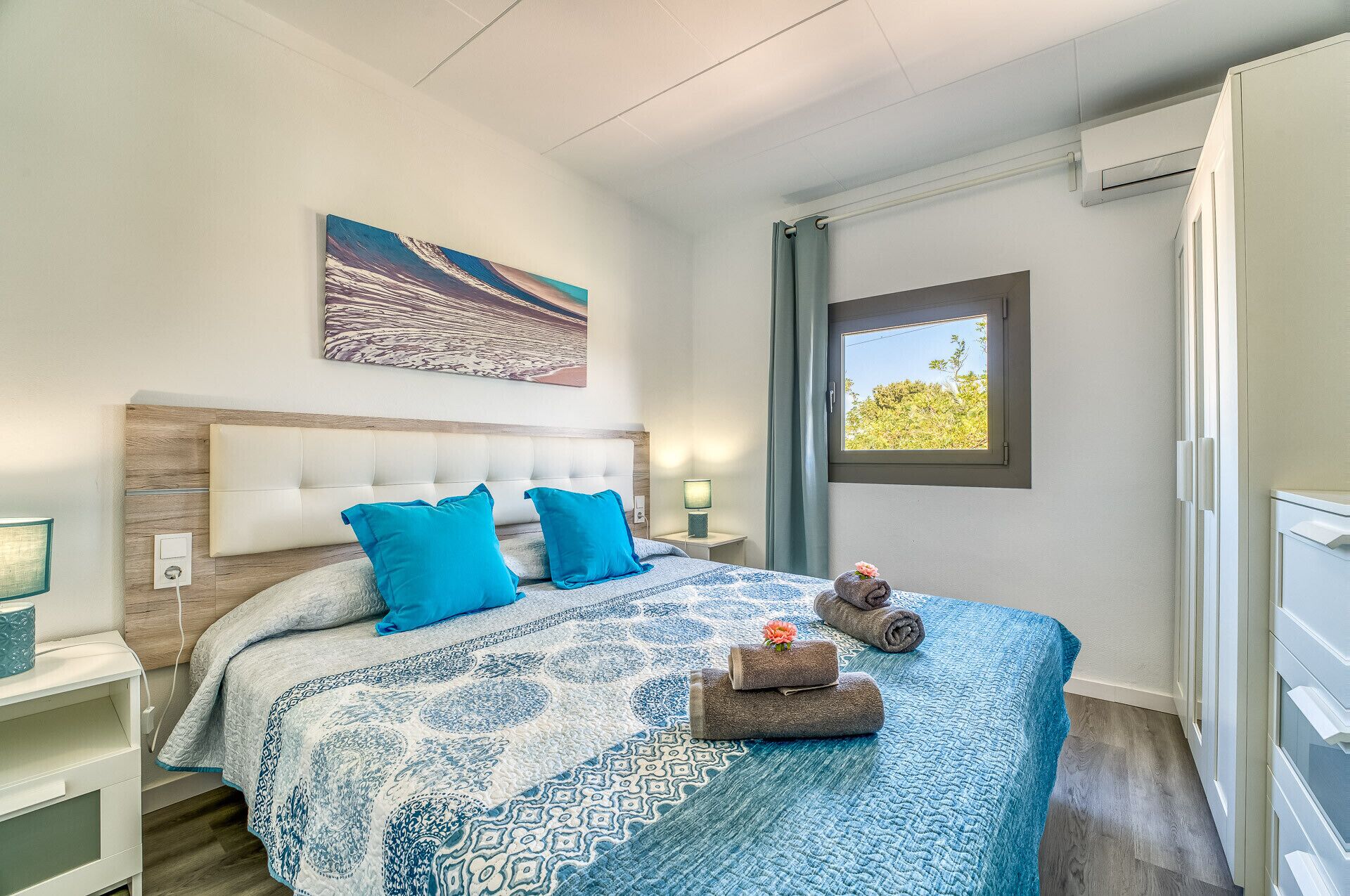 Une chambre à coucher avec un grand lit, une tête de lit, une table de chevet, une fenêtre donnant sur un beau paysage et un tableau accroché au mur.
