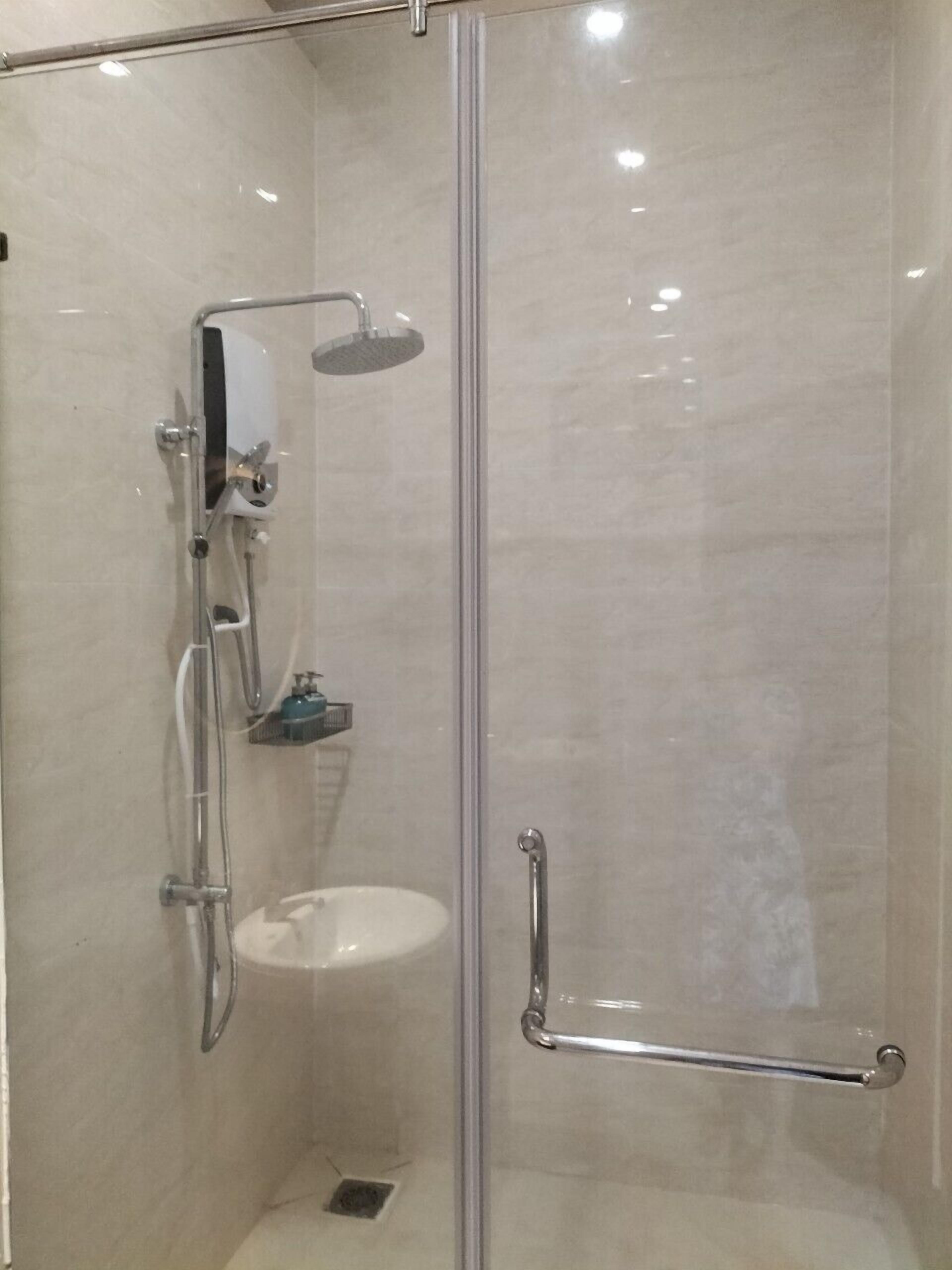 A glass-enclosed shower with a handheld showerhead, a handheld shower attachment, and a wall-mounted faucet.