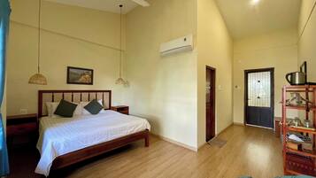 Un dormitorio con cama de madera, dos lámparas de noche, ventilador de techo, equipo de aire acondicionado y una puerta que da a otra habitación.