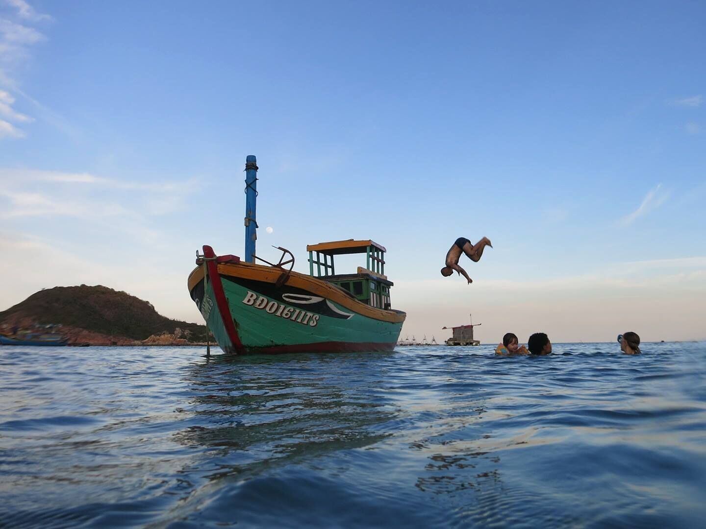 A boat named 'BDOIGTIS' anchored in calm waters with a clear sky and a distant hill.