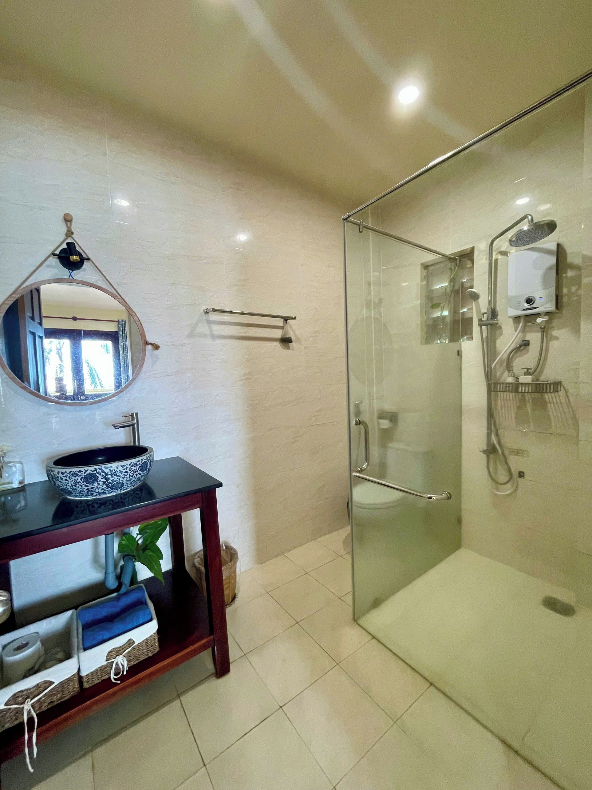 A modern bathroom with a glass-enclosed shower, a round mirror, and a vessel sink on a dark countertop.