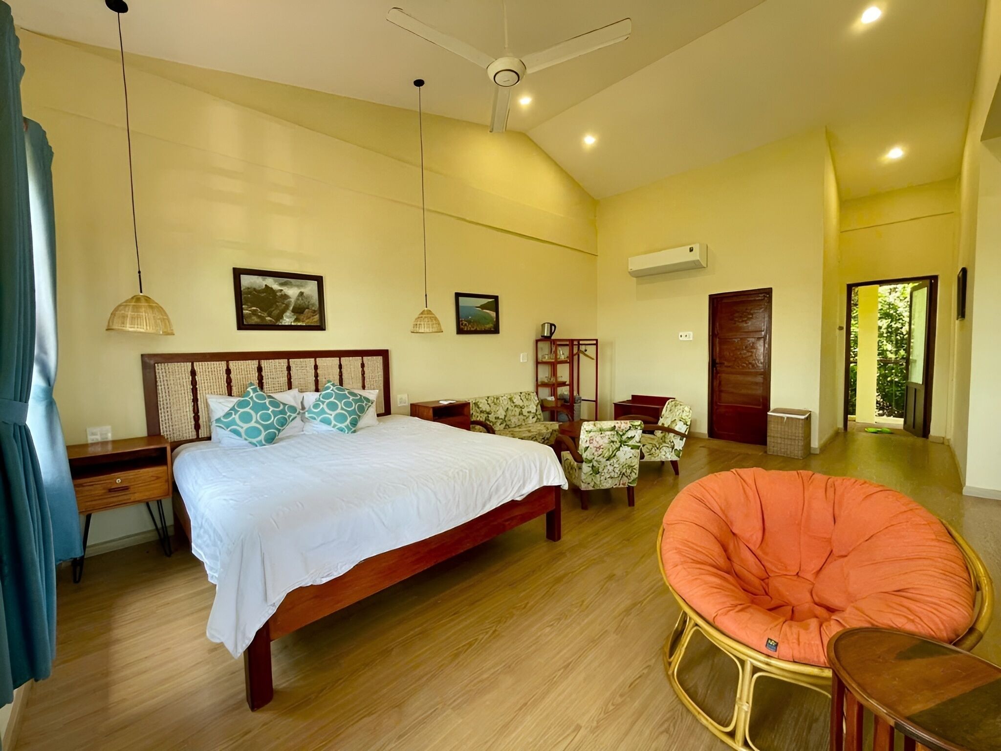 A spacious bedroom with a large bed, a sitting area with chairs, a ceiling fan, and a view of the outdoors.
