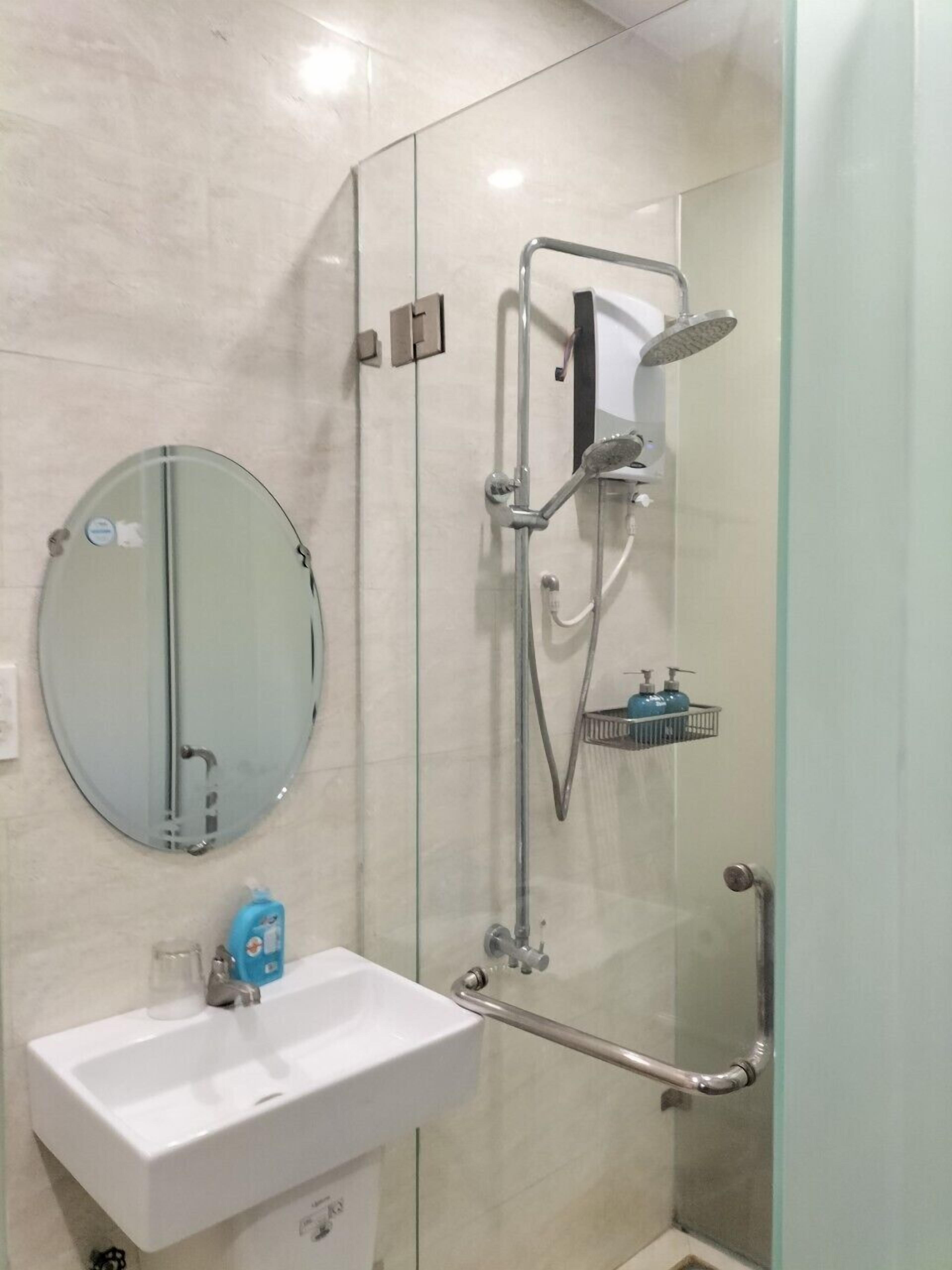 Ein Badezimmer mit einer Duschkabine, einem runden Spiegel und einem weißen Waschbecken.