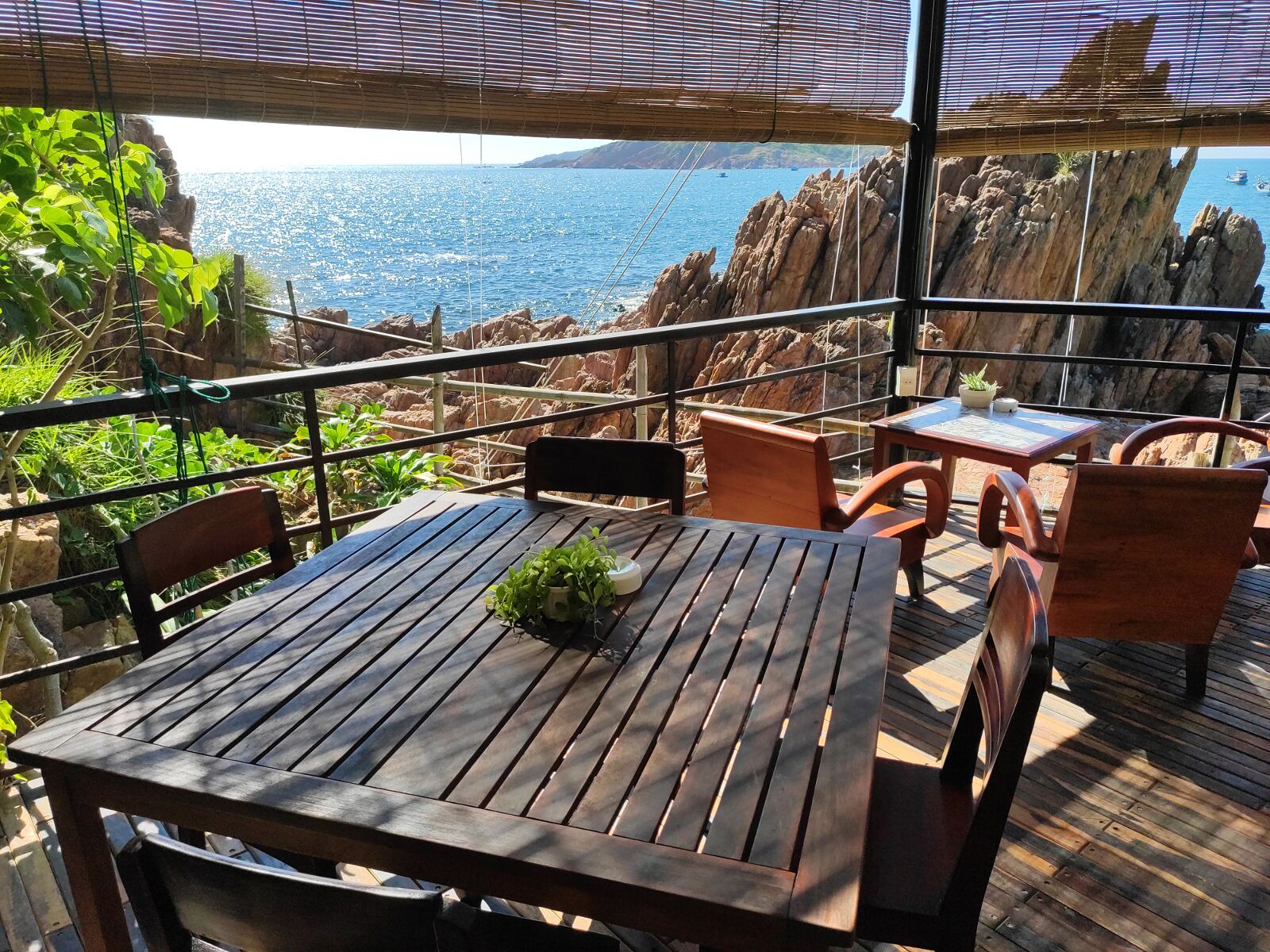 Een terras van hout buiten, met een tafel en stoelen, met uitzicht op een rotsachtige kustlijn en de zee.