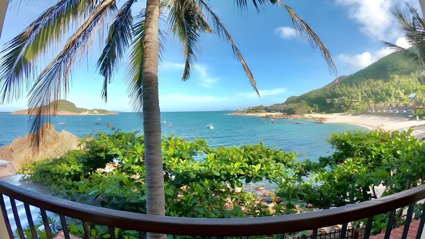 A balcony with a view of a beach, palm trees, and the sea. - Haven Boutique Hotel Quy Nhon (Quy Nhon Nam)