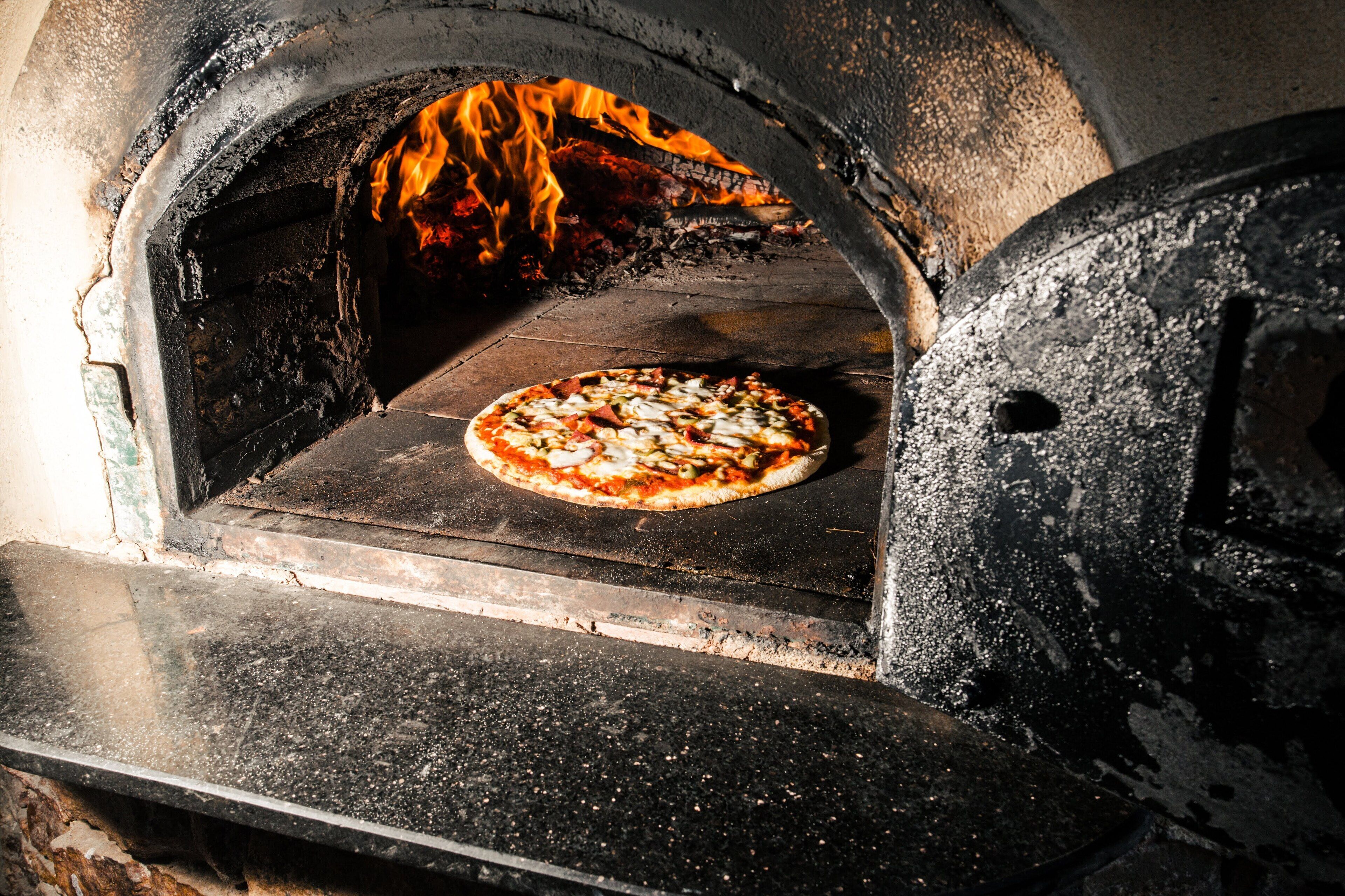 A pizza inside a wood-fired oven with flames visible.