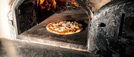 A pizza inside a wood-fired oven with flames visible.
