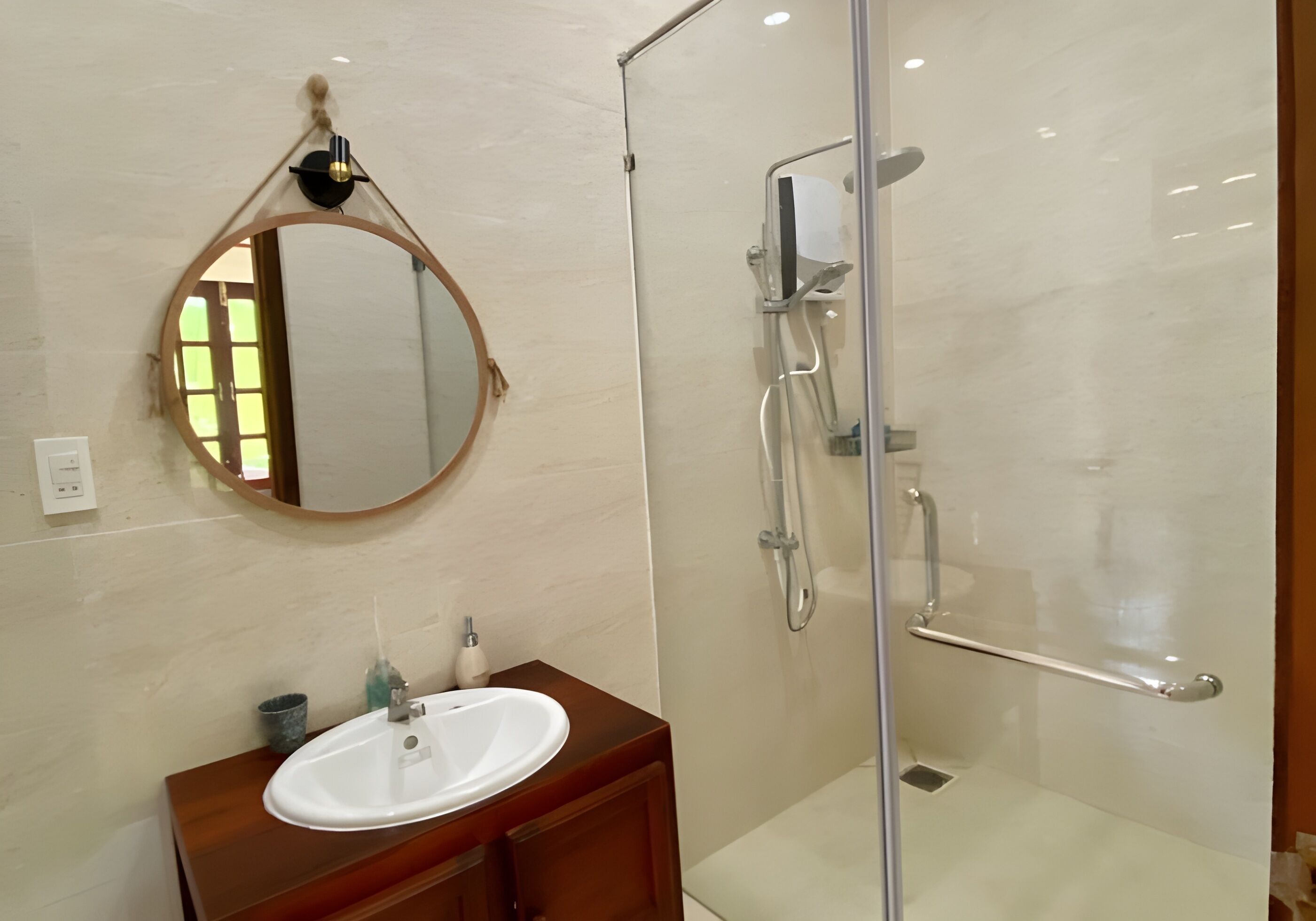 Un baño con un espejo redondo, un lavamanos y una zona de ducha con paredes de vidrio.