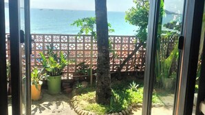 A glass door leading to a balcony with a view of the sea, a palm tree, and potted plants. - Haven Boutique Hotel Quy Nhon (Quy Nhon Nam)