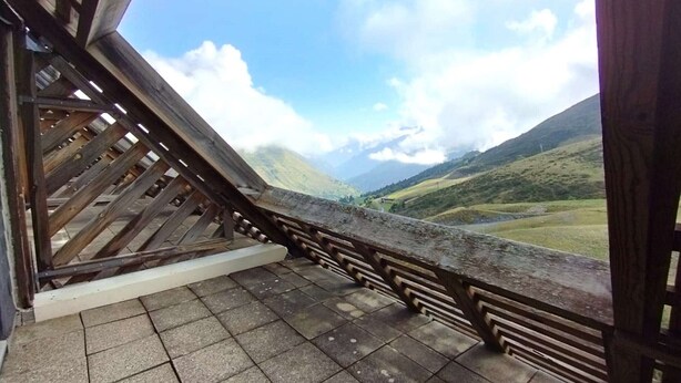 A wooden balcony with a tiled floor, overlooking a mountainous landscape.