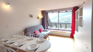 A dining area with a table set for four, a sofa with red cushions, and a view of a mountainous landscape through large windows.