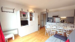 A compact living space with a kitchenette, dining area, and a sofa with a red pillow.