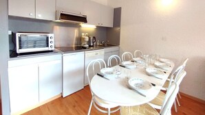 A compact kitchen with a microwave, coffee maker, and dishwasher. There is a dining table set with plates, glasses, and cutlery.