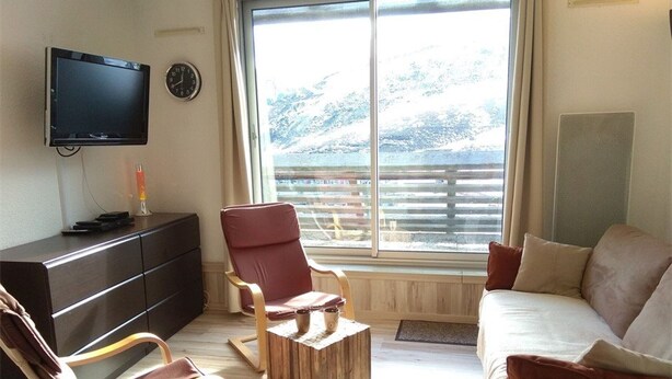 Un salon avec une télévision, un fauteuil rouge, une table basse en bois et un canapé avec des coussins.