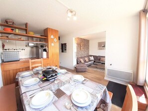A dining area with a table set for four, a kitchen with wooden cabinets, and a living room with a sofa and a fireplace.