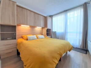 A bedroom with a bed, built-in shelving, a window with curtains, and a ceiling light.