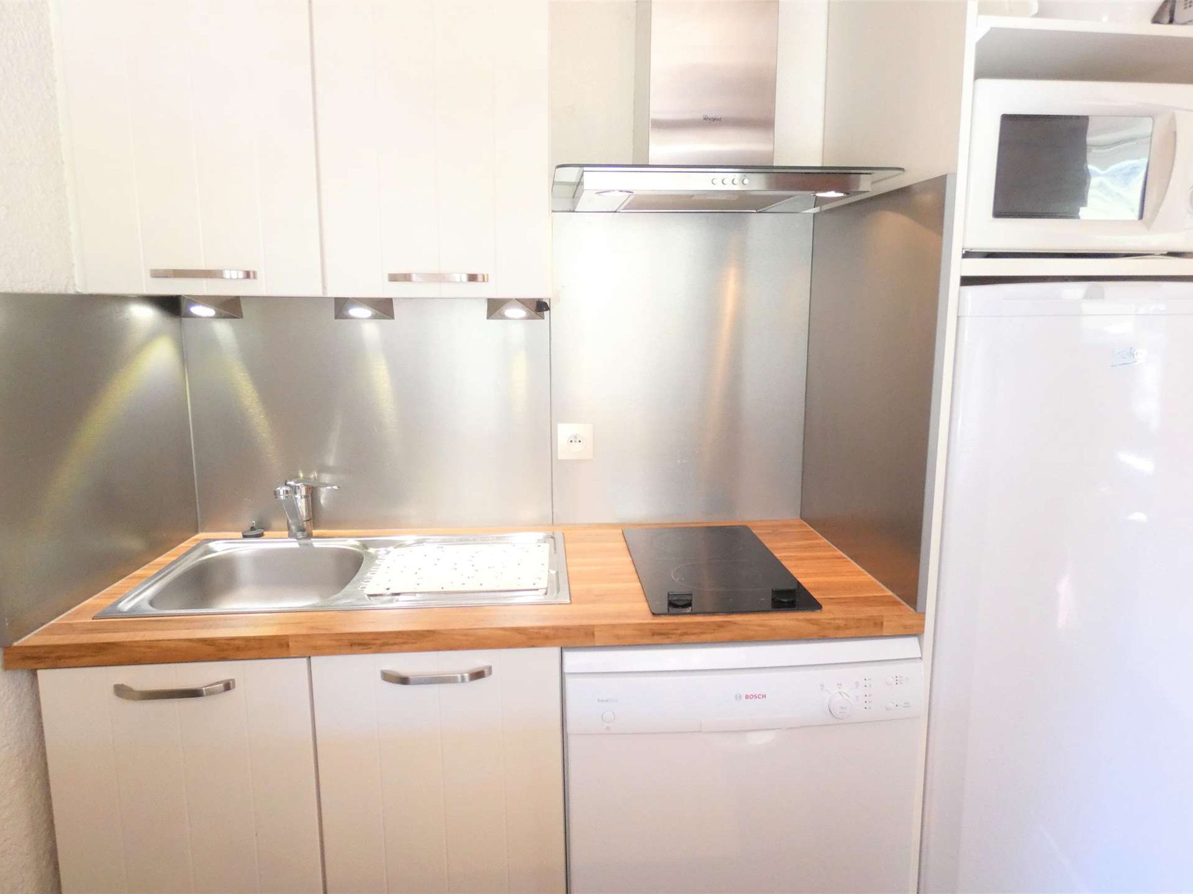 A compact kitchen with a stainless steel sink, wooden countertop, white cabinets, a Bosch dishwasher, and a microwave.