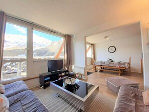 Ein Wohnzimmer mit einer Couch, einem Couchtisch, einem Fernseher und einem Essbereich mit Tisch und Stühlen.