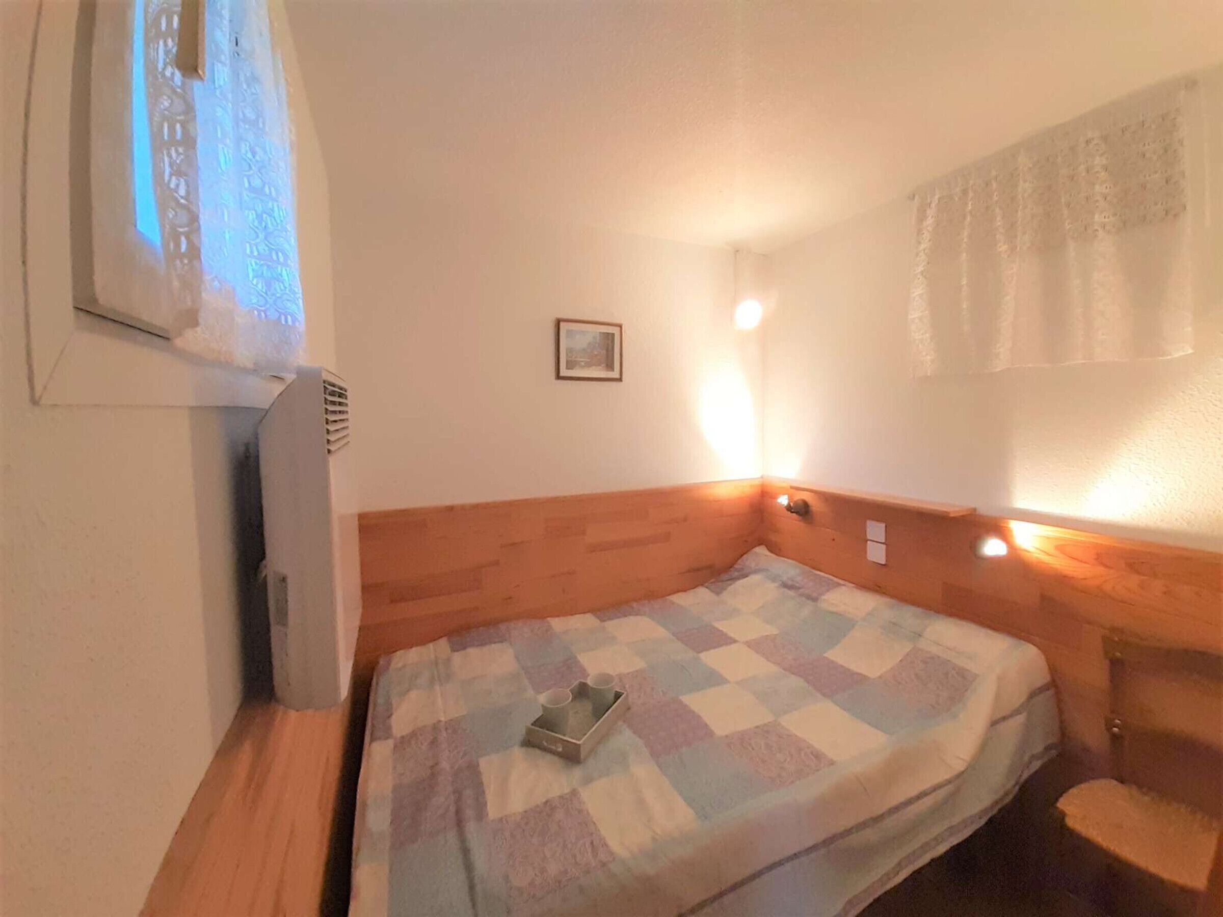 A small, cozy room with a single bed, a window with a view, and a wall-mounted light fixture.