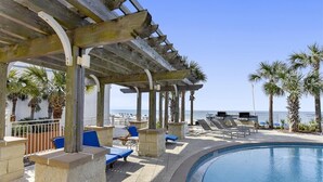 A poolside area with lounge chairs, a pergola, and palm trees.