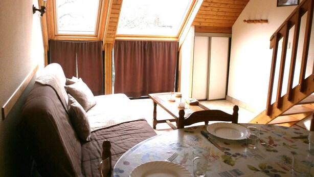 Ein gemütliches Zimmer mit einem Bett, einem Esstisch für zwei Personen und einem großen Fenster mit viel Tageslicht.
