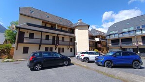 Ein mehrstöckiges Gebäude mit Balkonen, ein Parkplatz mit mehreren Autos und ein klarer, blauer Himmel.